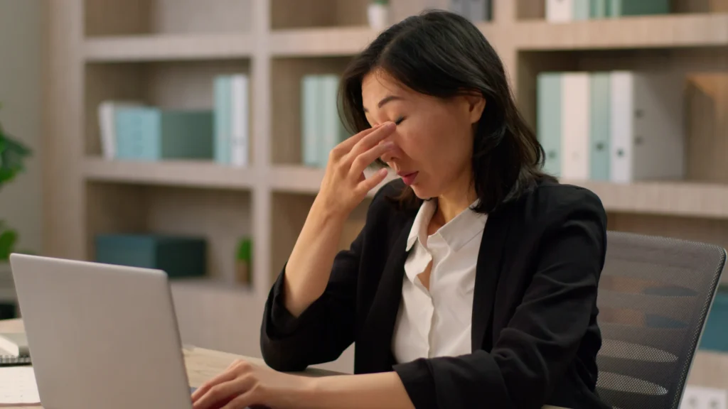 デスクワークで頭痛に悩んでいる女性の画像。